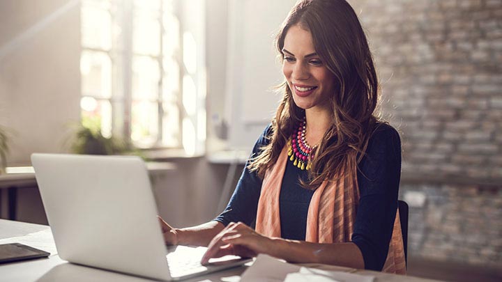 Wanita tersenyum duduk mengetik di laptop